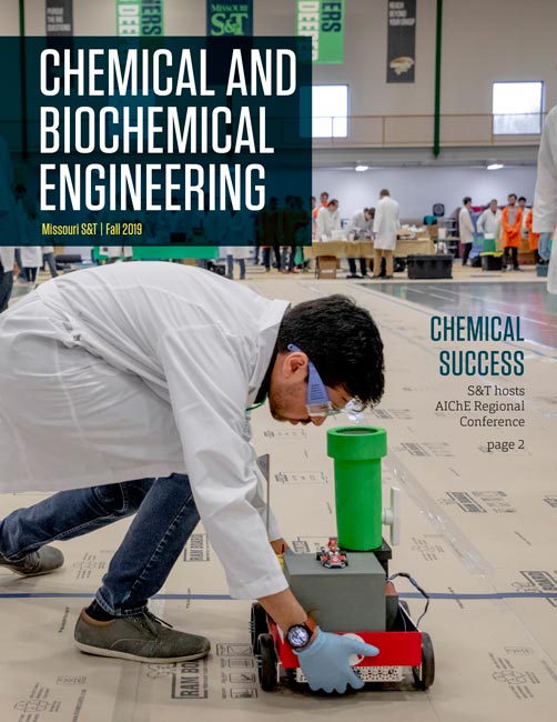 Newsletter cover title in white text with student standing in the gym wearing a lab coat, goggles and gloves adjusting a chemical reactive shoebox-sized car.